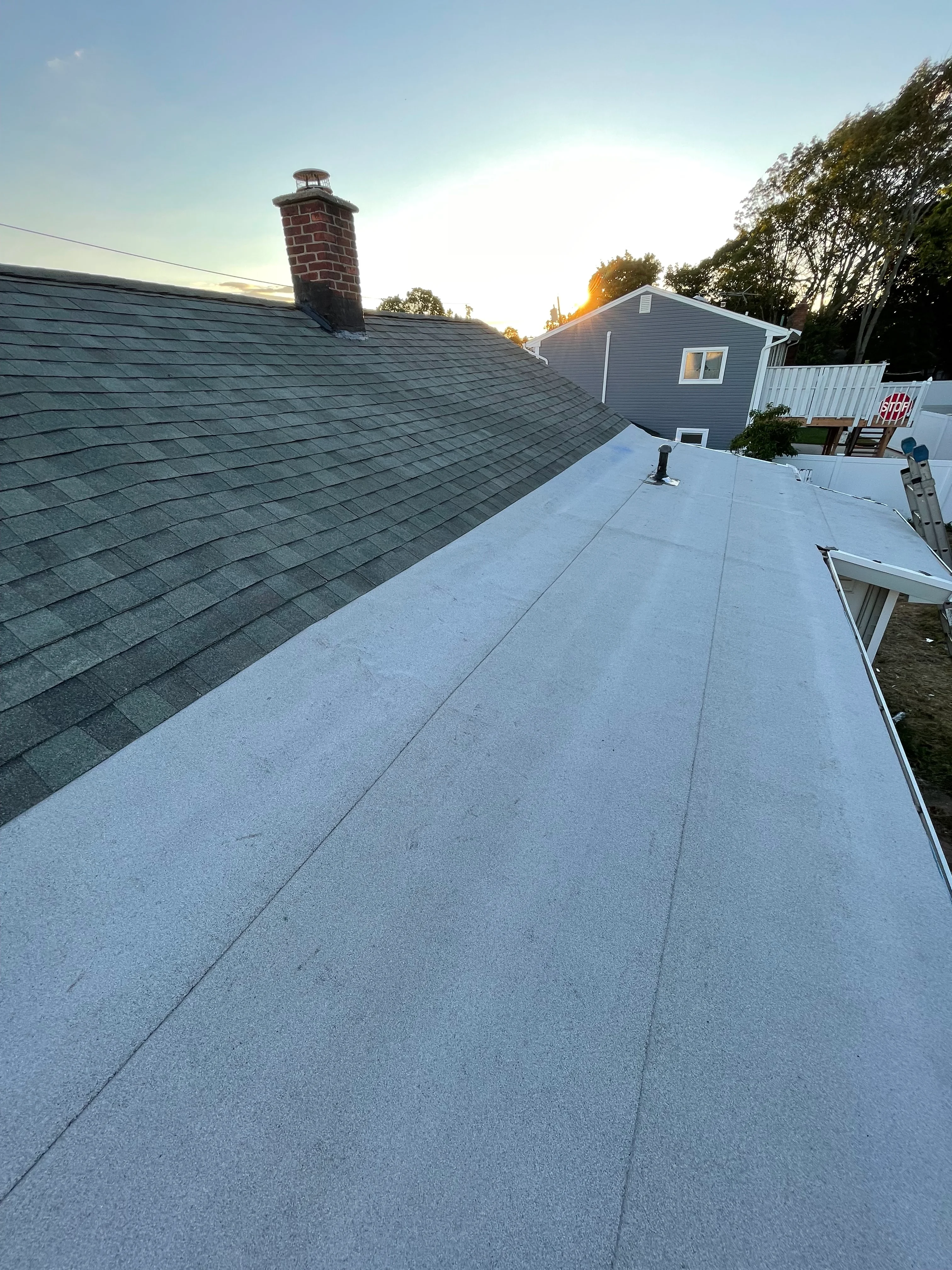 Newly installed white flat roof and dark asphalt shingle roof on residential home with brick chimney