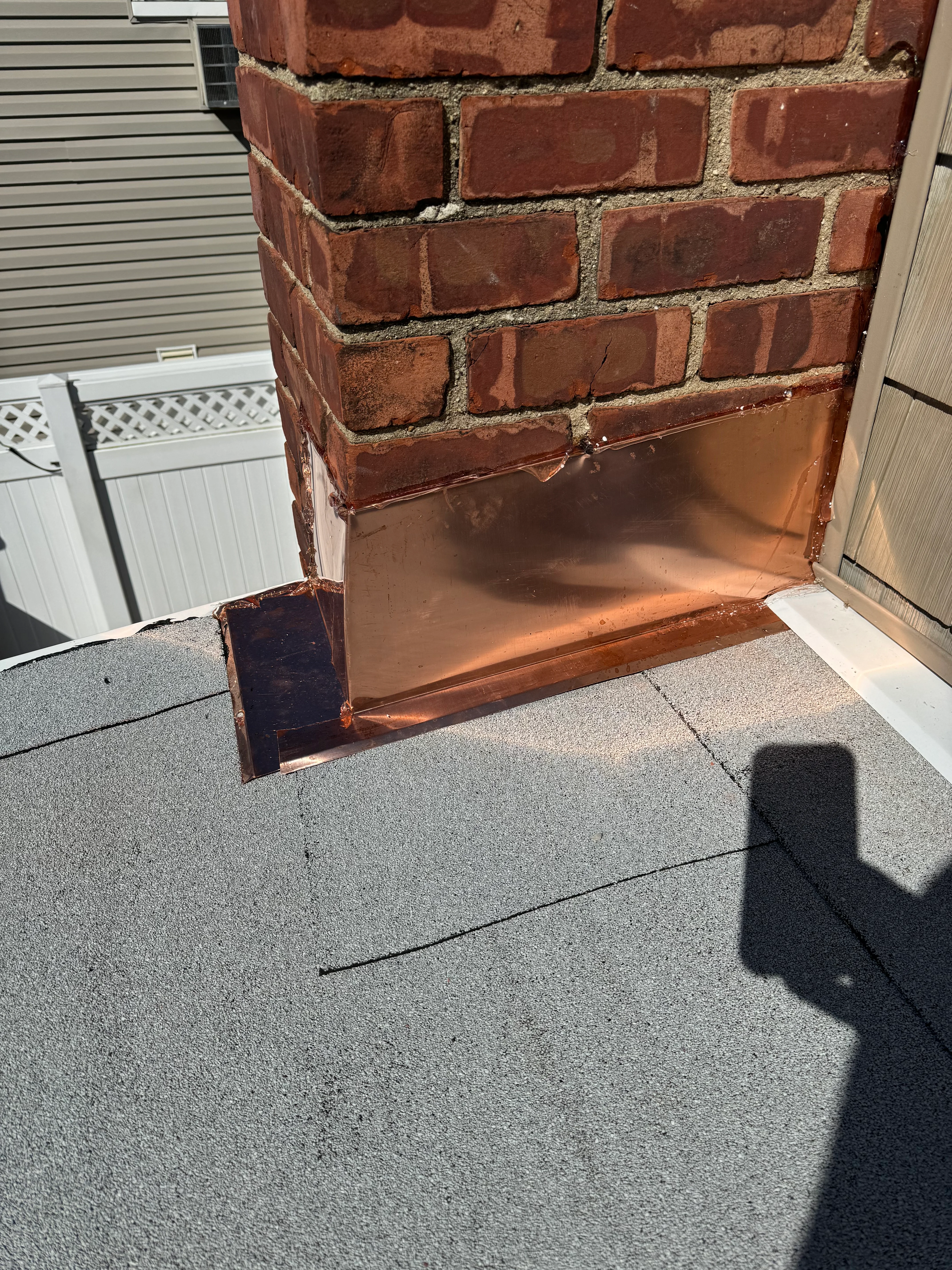 Copper flashing installed at brick chimney roof transition with asphalt shingles
