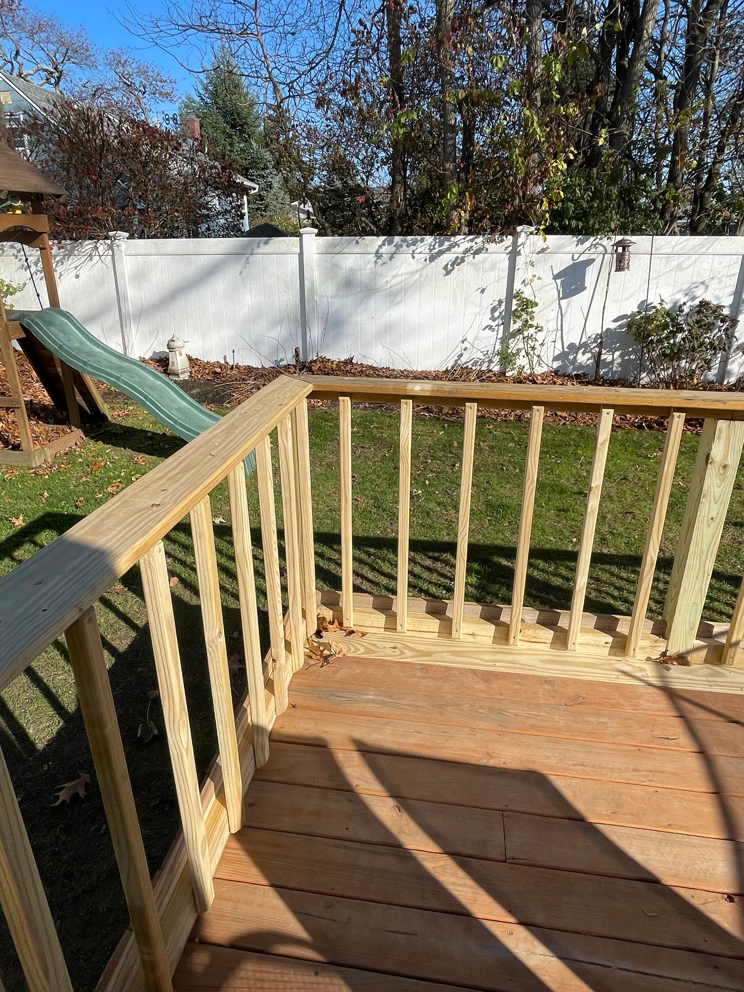 New wood deck with railings and white vinyl privacy fence in residential backyard