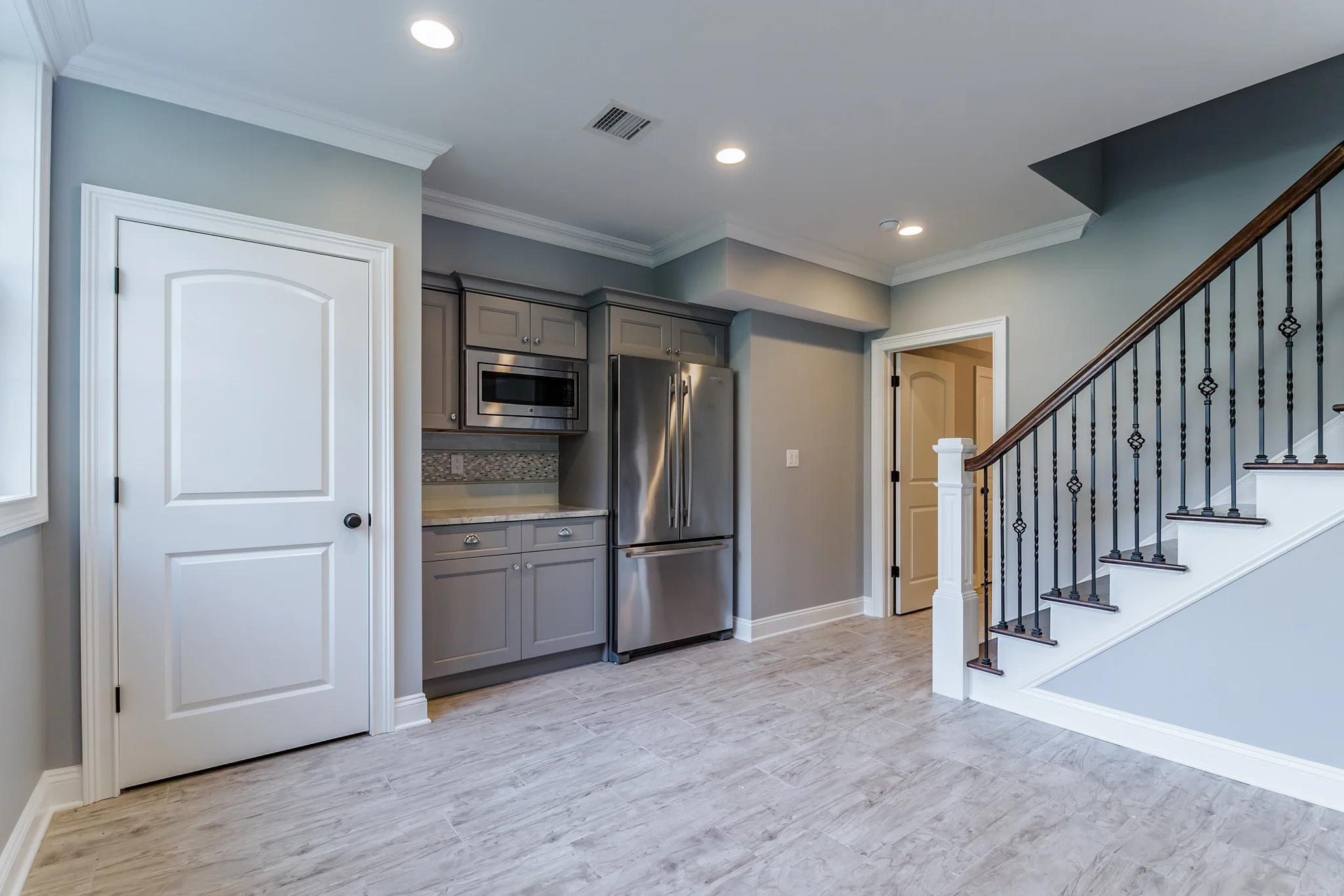 Modern kitchen with gray cabinetry and stainless appliances adjacent to staircase with metal railings