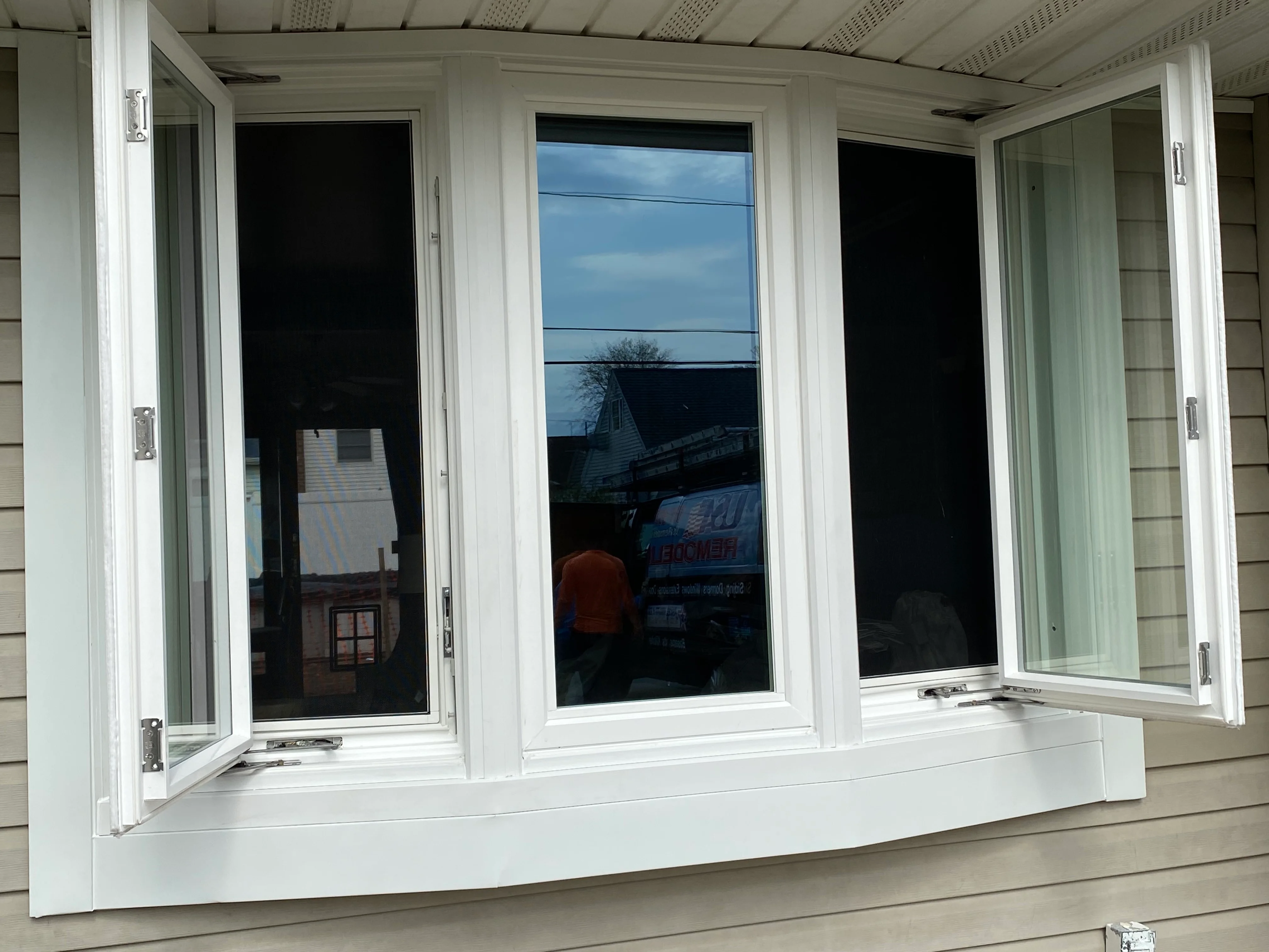 Three white vinyl casement windows with black glass and matching trim installed on residential siding