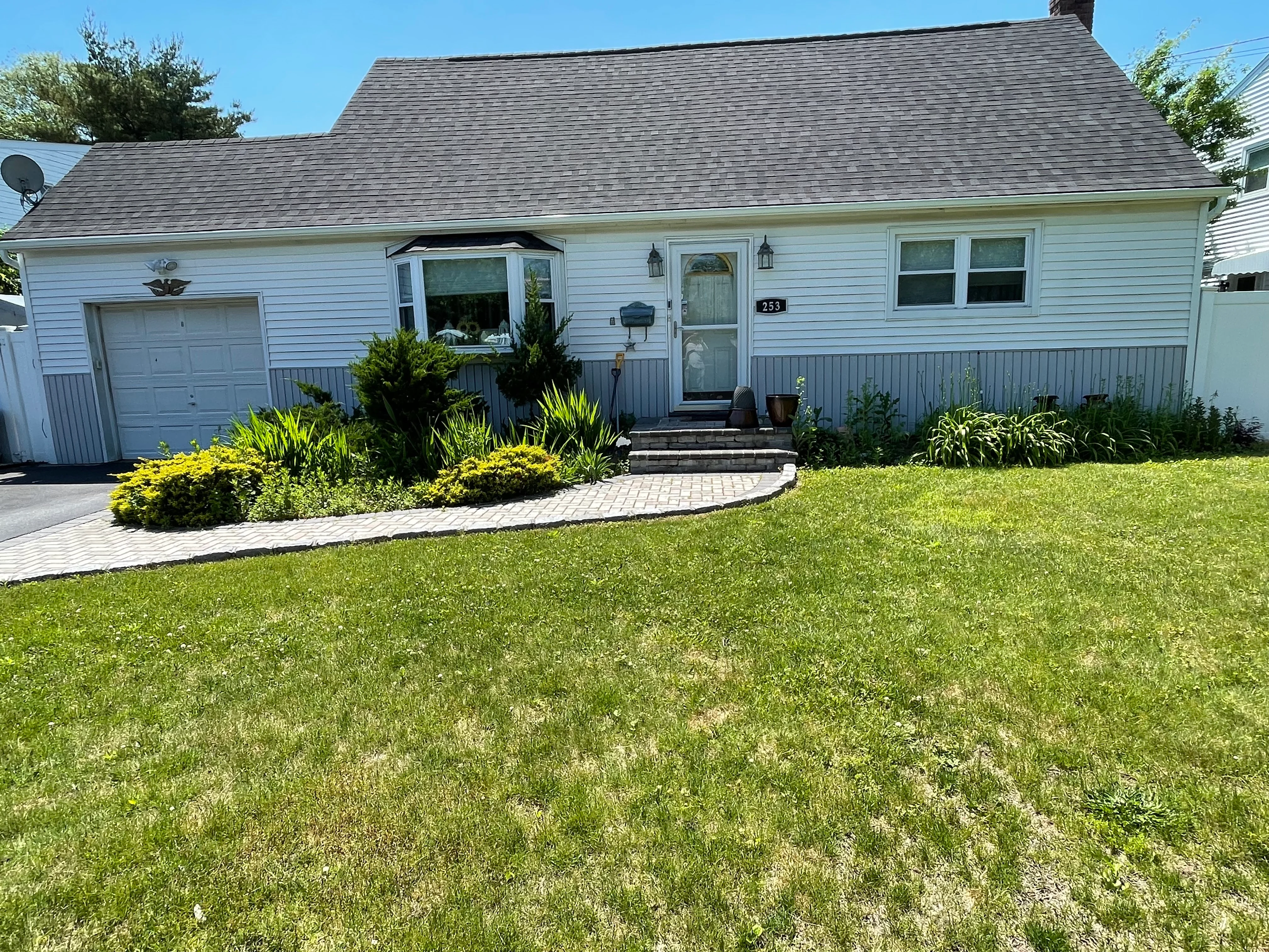 White ranch home with new siding, gray roof, paver walkway, and landscaped front yard