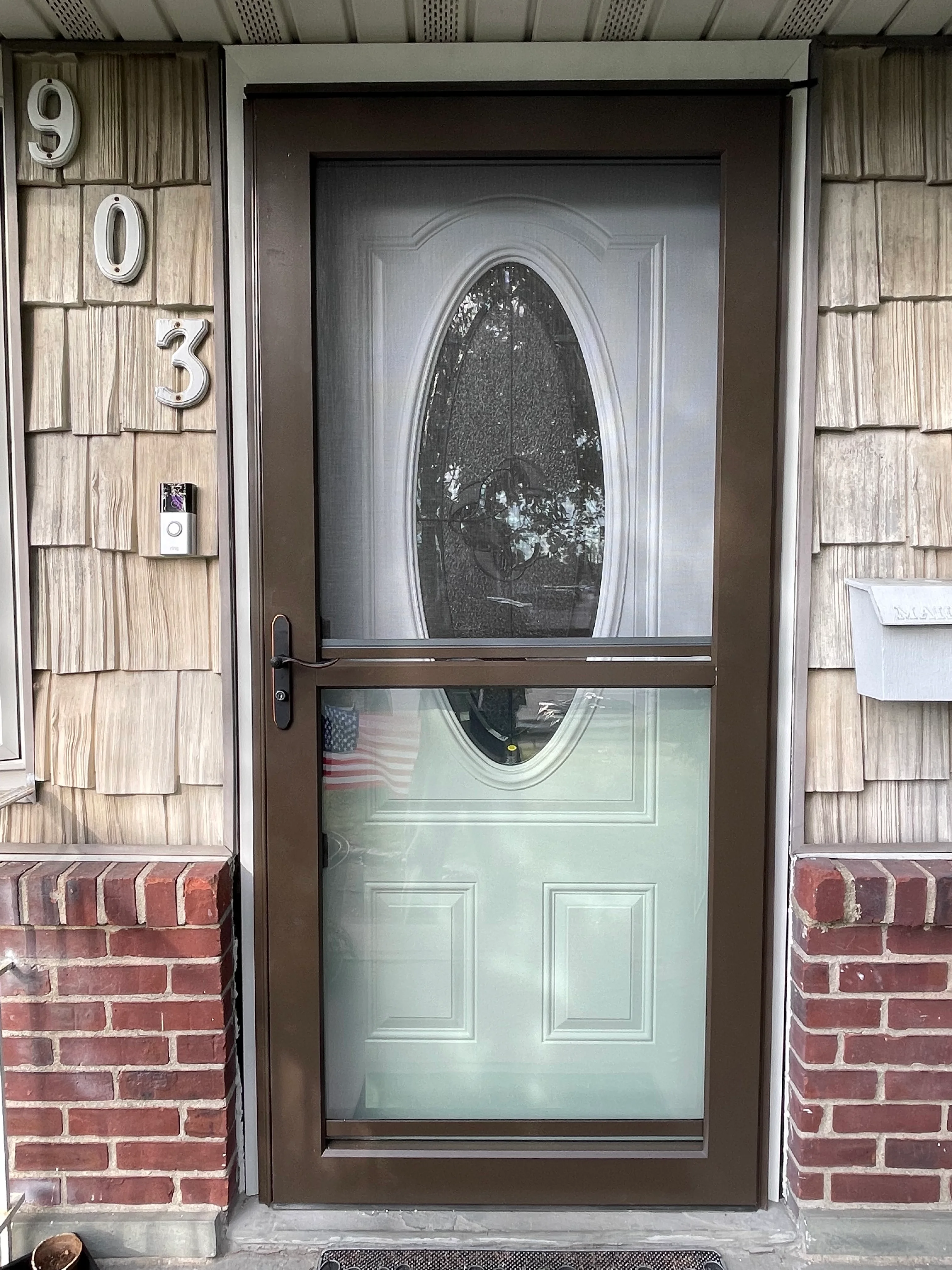 Bronze storm door with oval glass panel installed on brick and cedar shake home exterior