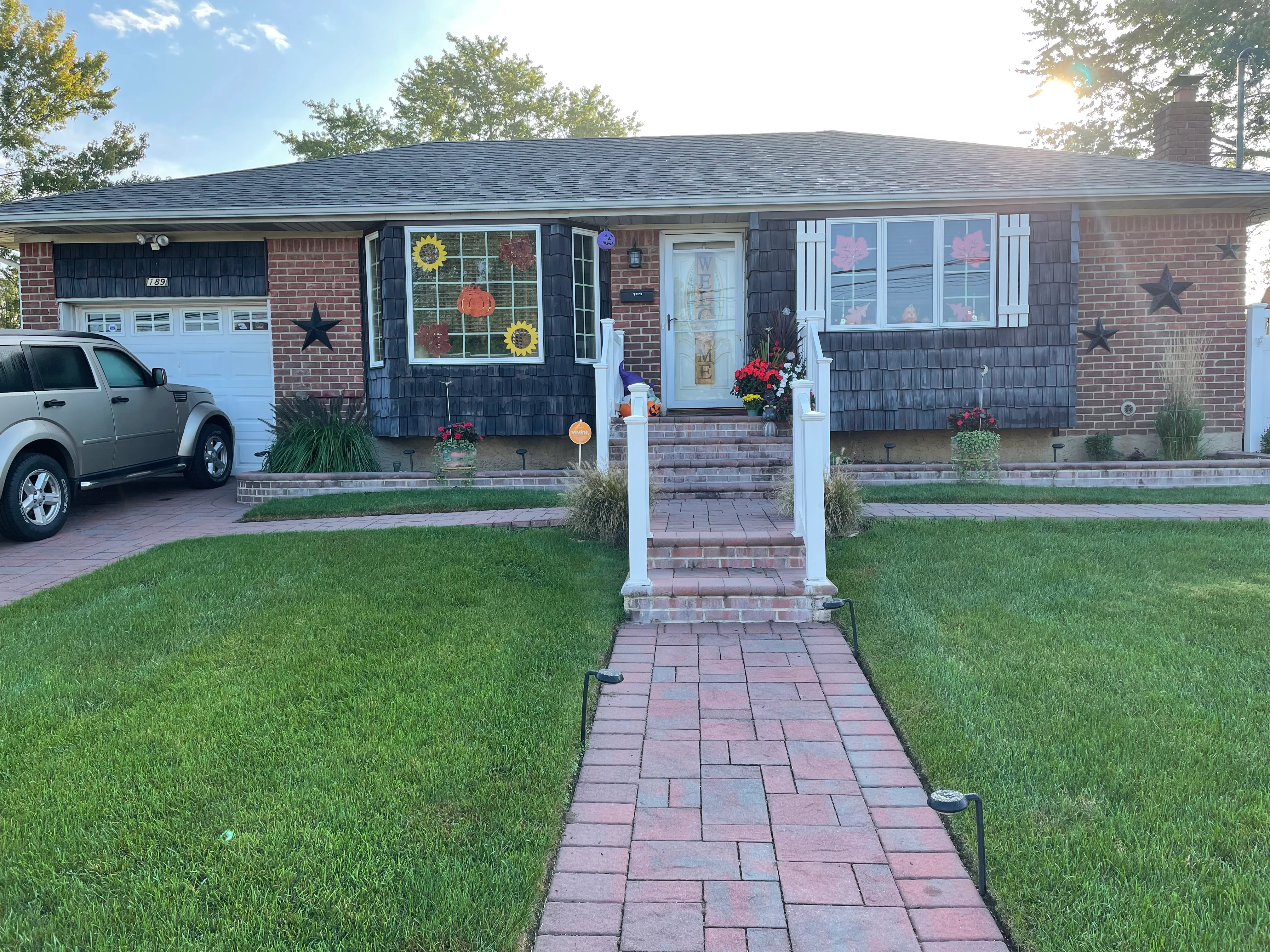 Brick ranch home with new black roof, dark siding, white entry gate, and brick walkway