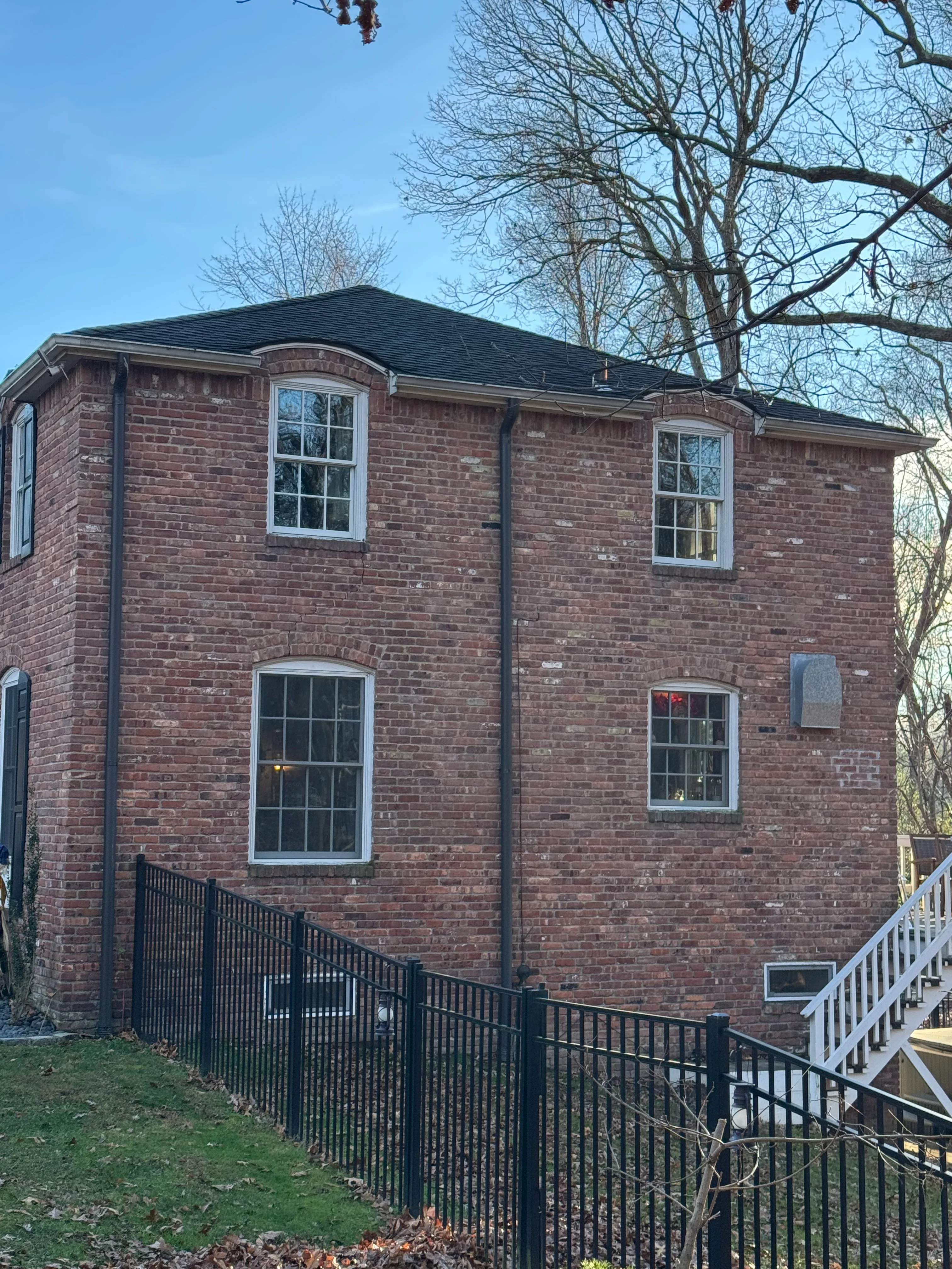 Two-story brick home with new dark roof, white-trimmed windows, and black metal railings