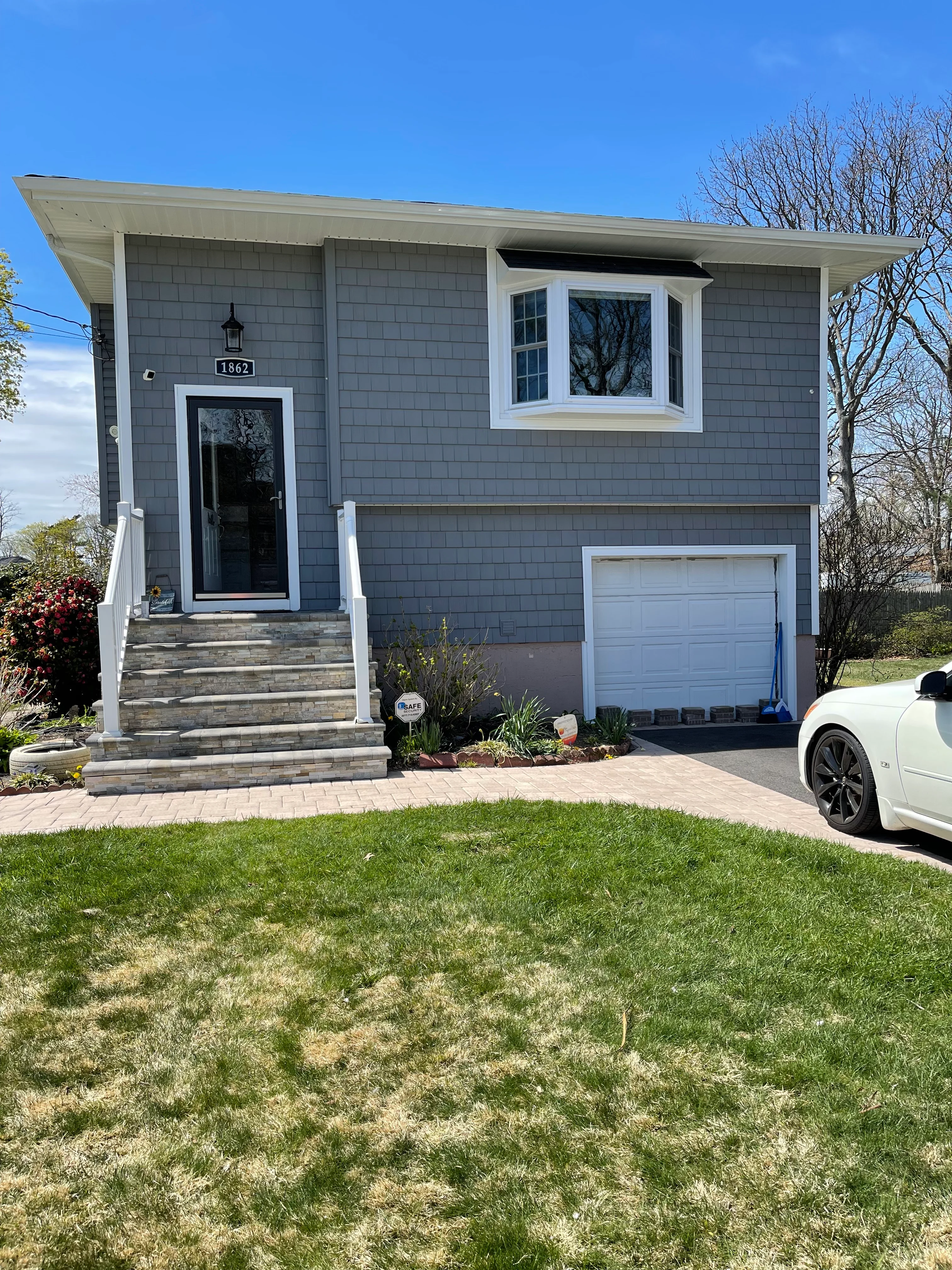 Modern two-story home with gray siding, white bay window, and new brick driveway