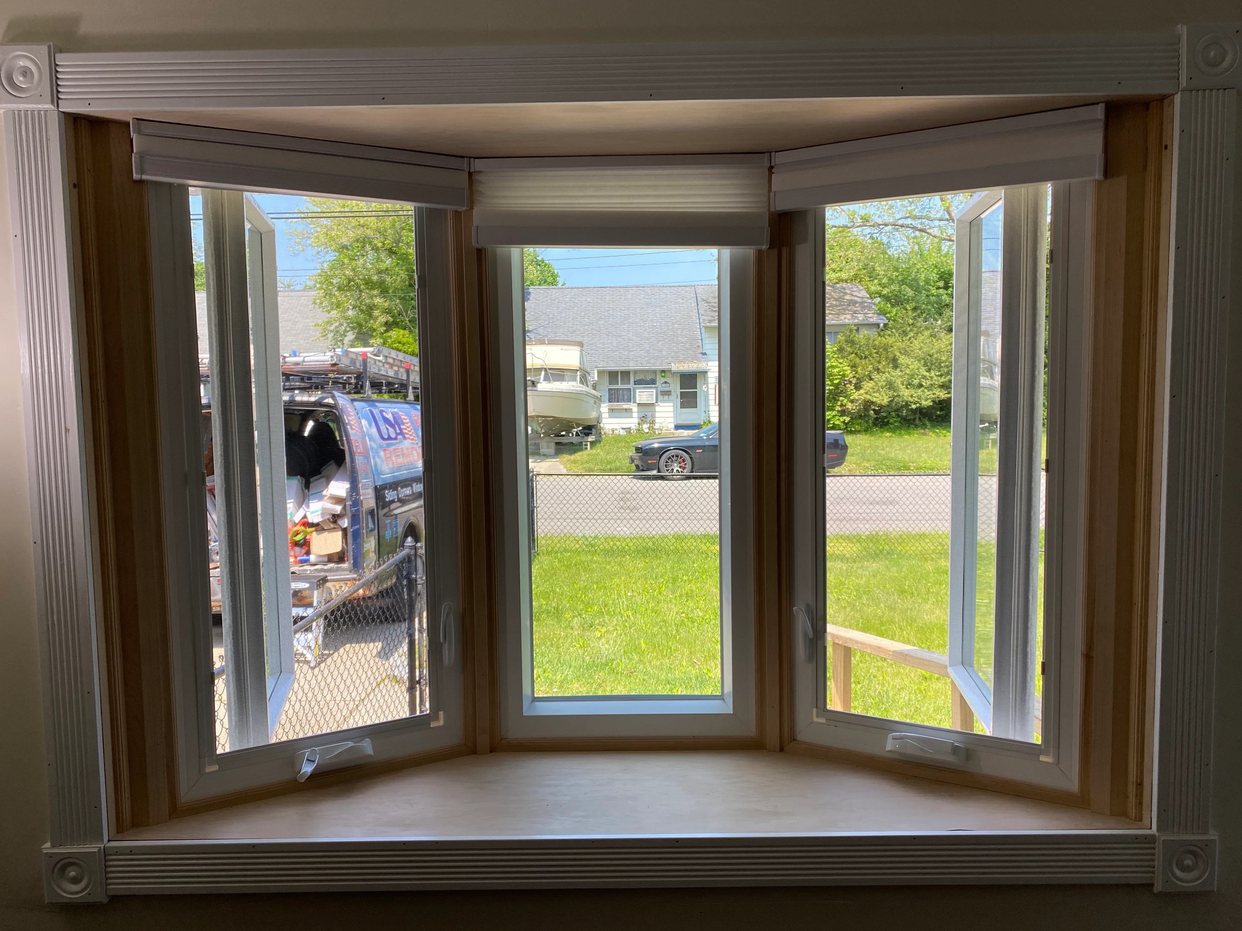 Three-panel bay window with motorized shades overlooking residential yard and street