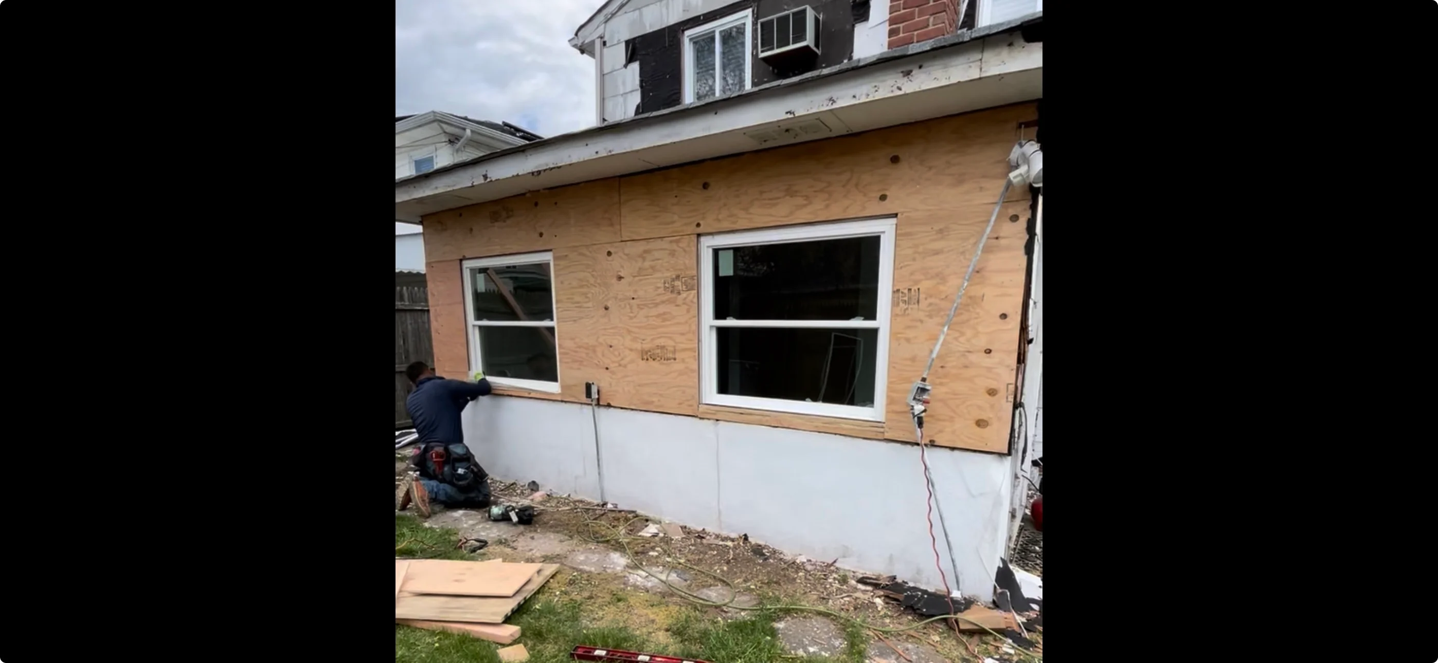 New home addition with two white-framed windows in OSB sheathing and white foundation wrap
