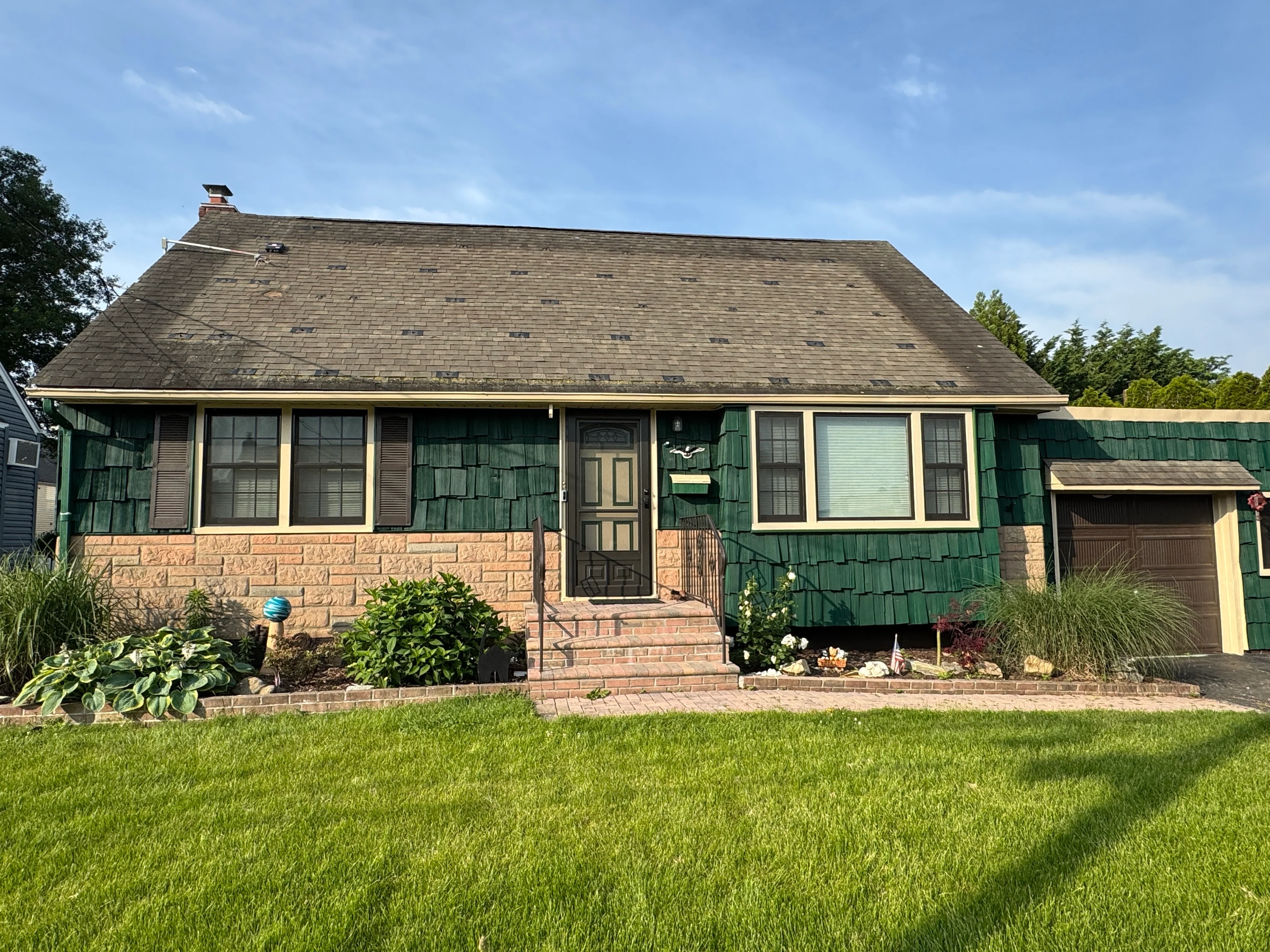Renovated ranch home with new green siding, roof, windows, and brick foundation in Lindenhurst