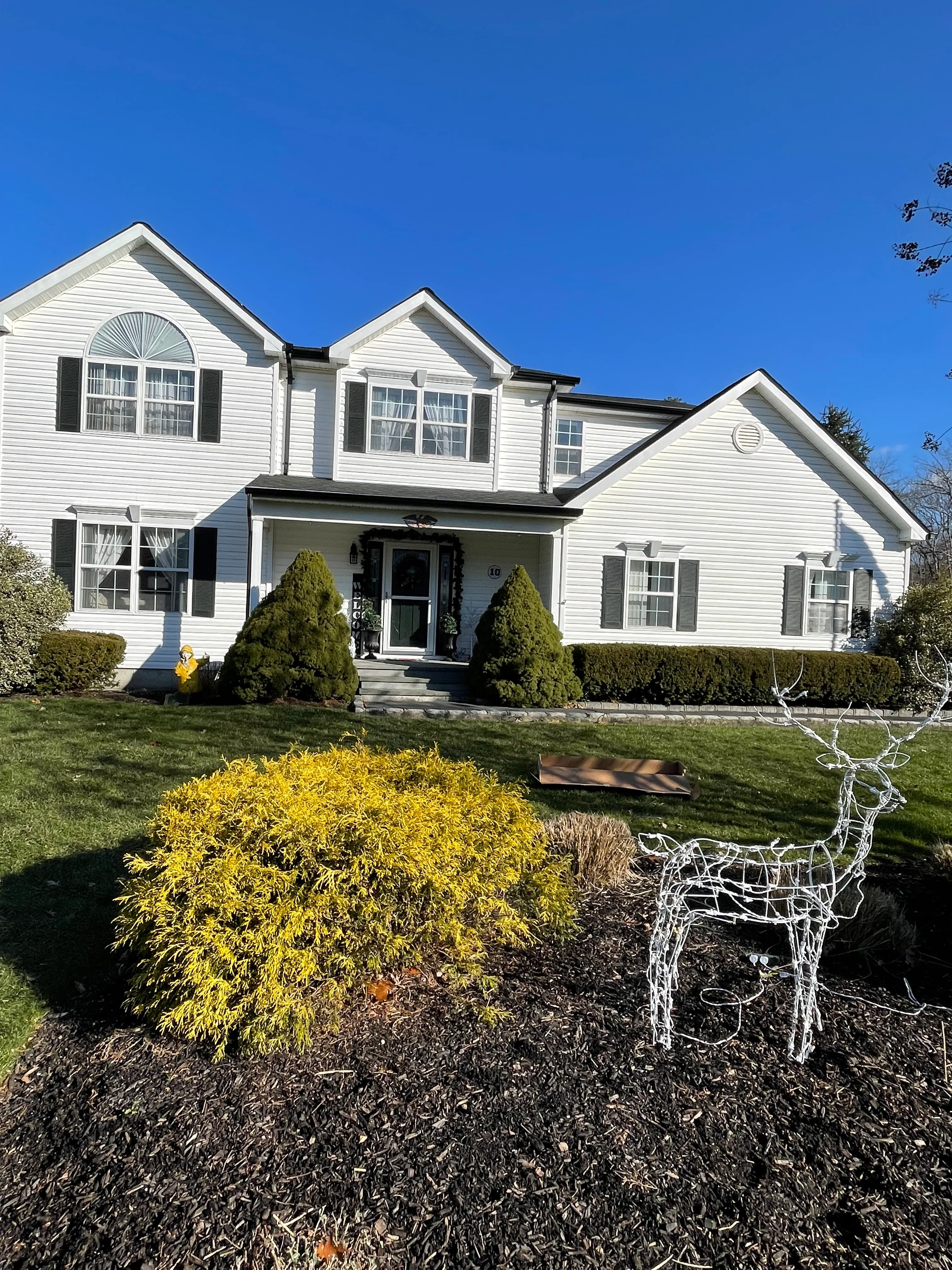 White colonial home with black shutters, new vinyl siding, and landscaped front yard