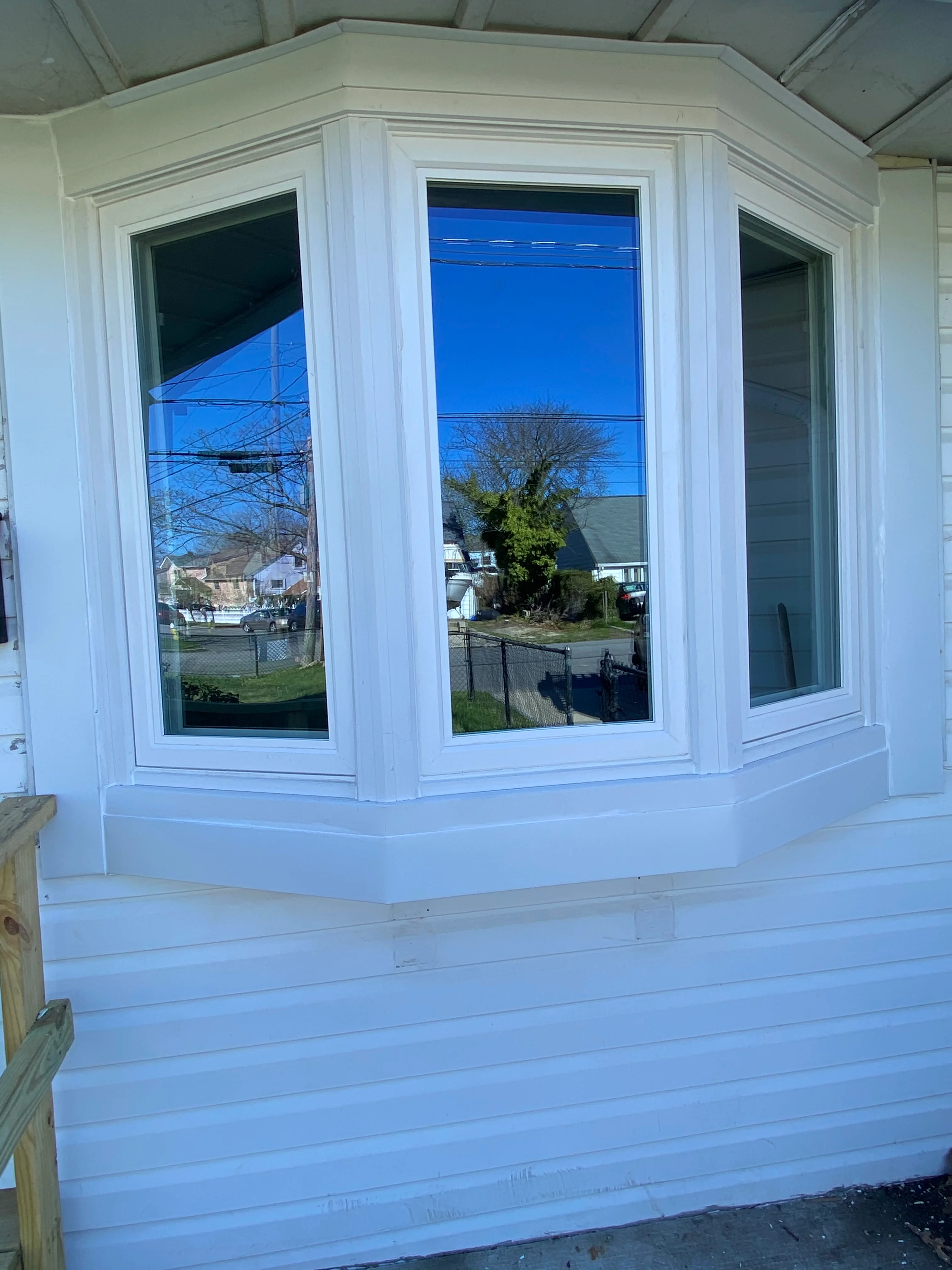Three-window bay installation with white trim and wood paneling on residential home