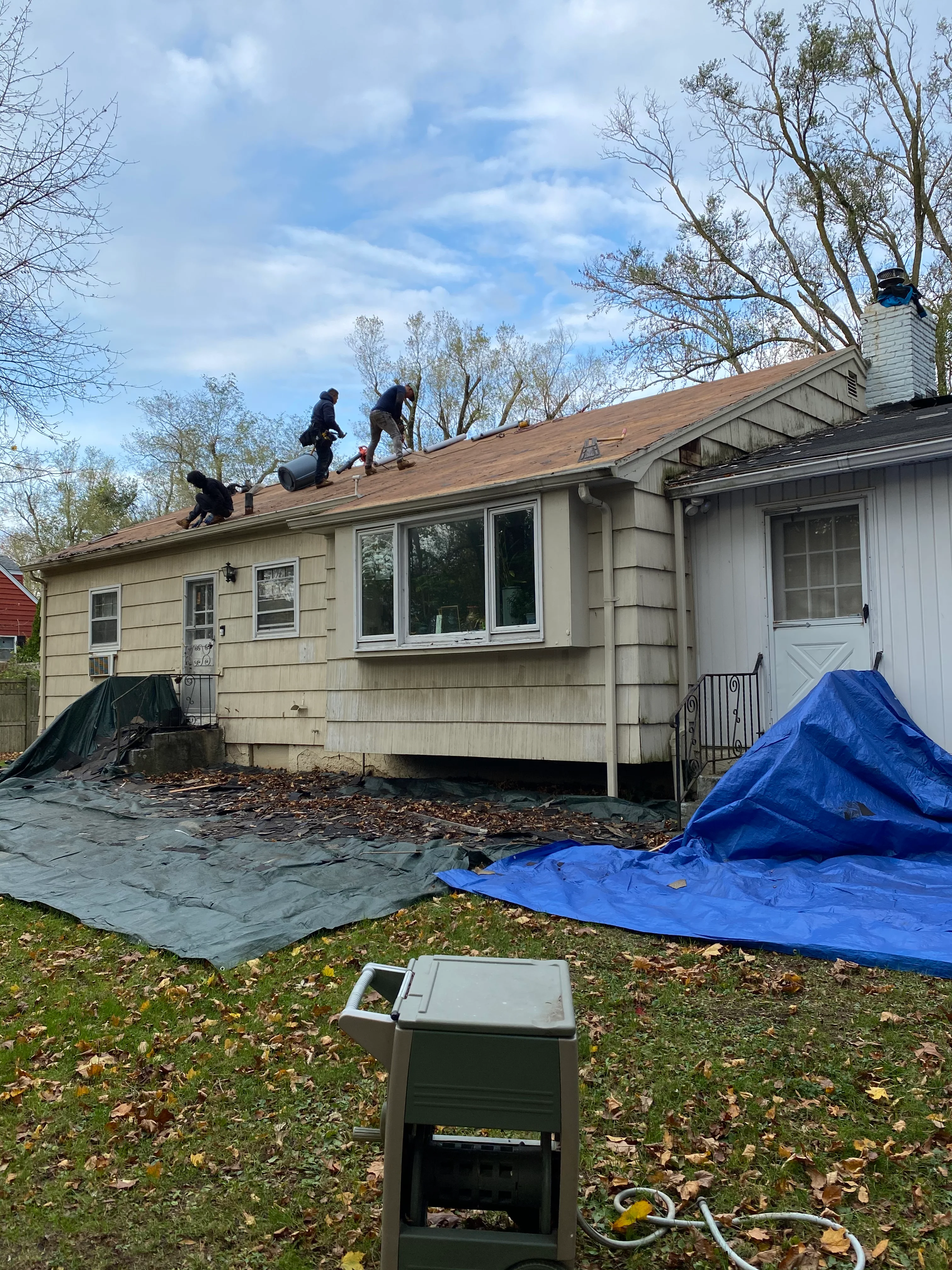 Roofing crew installing new asphalt shingles on residential home roof in Lindenhurst