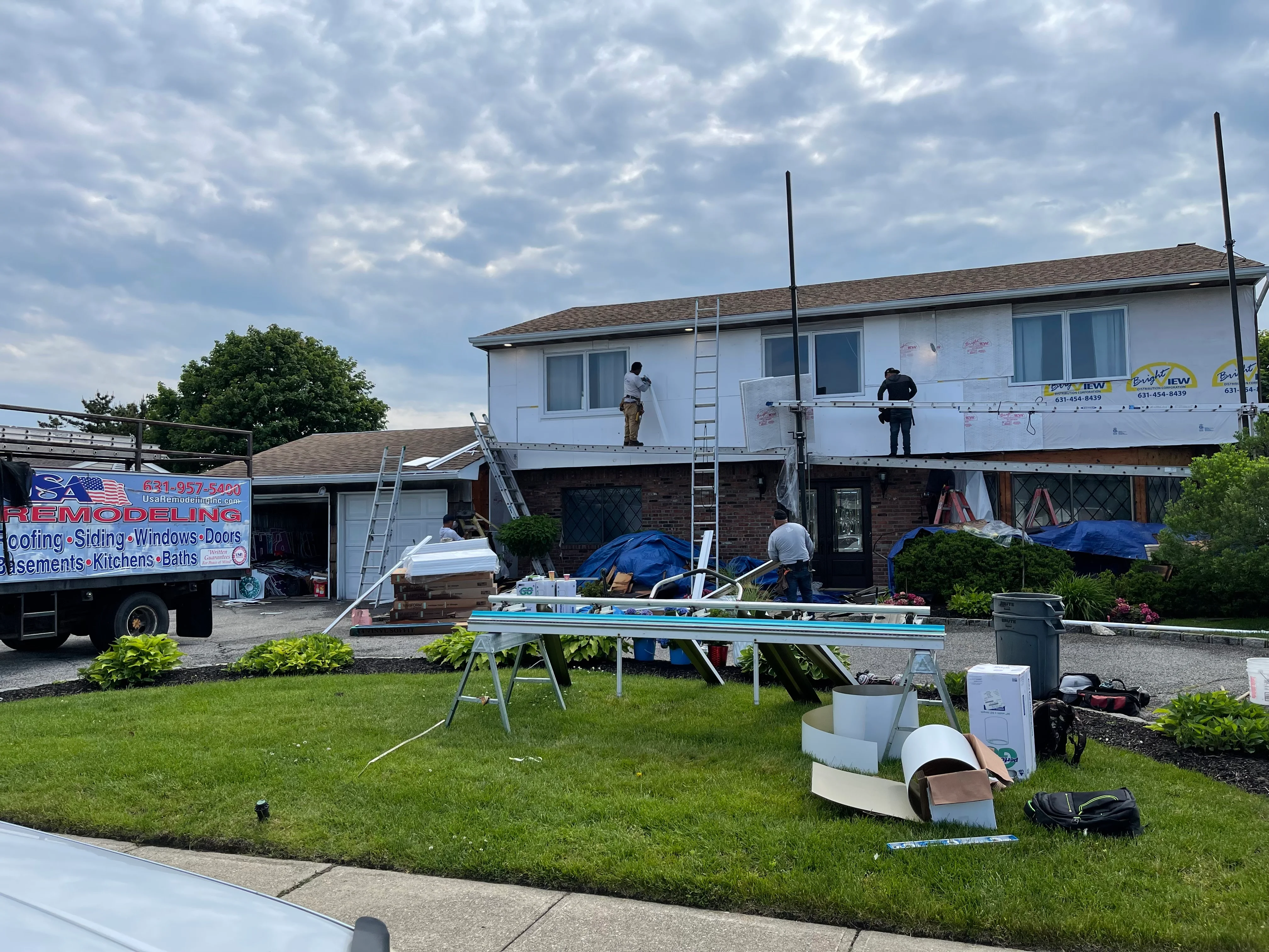 Raised ranch home undergoing exterior renovation with workers on roof and siding installation in progress