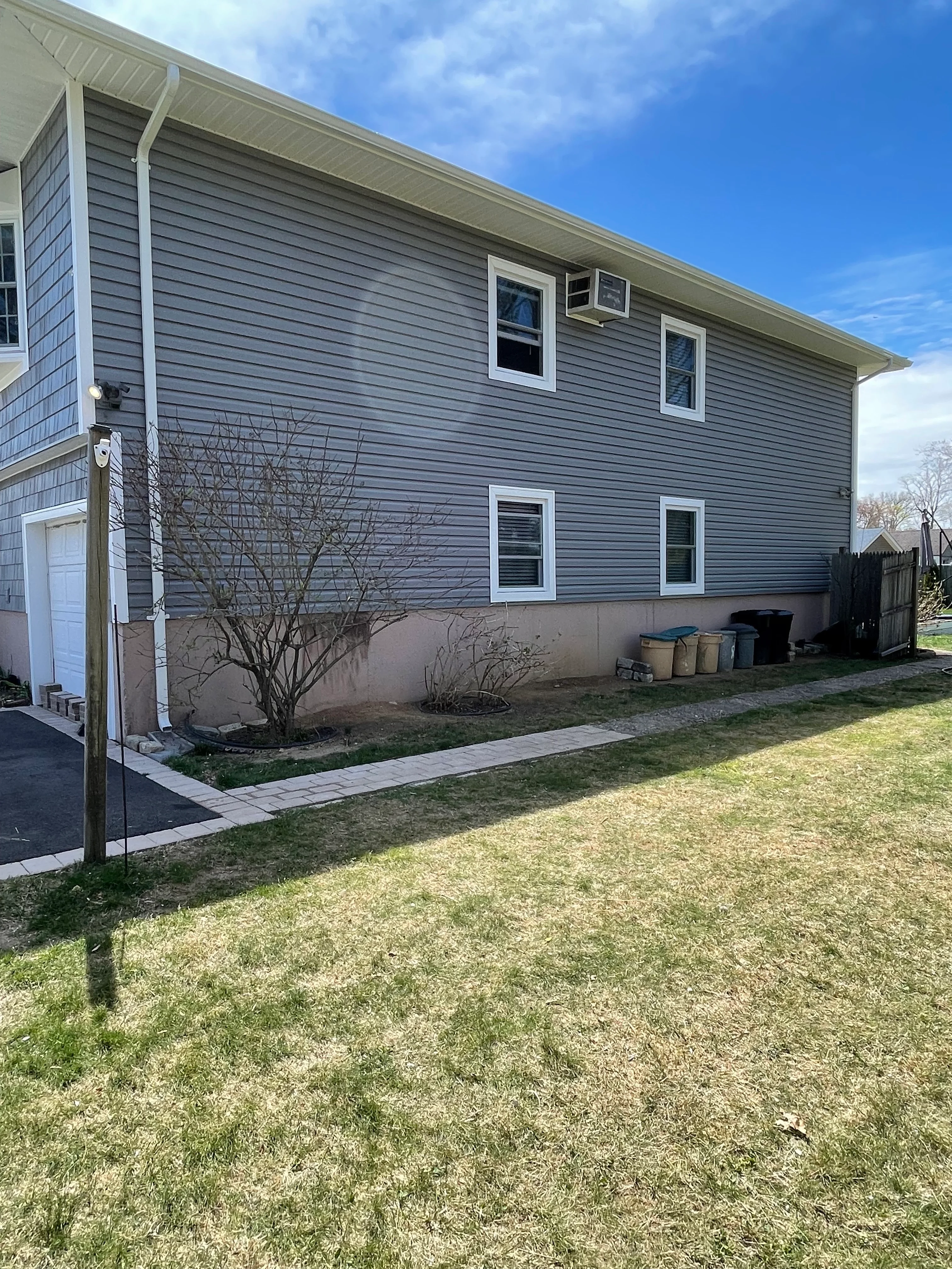 Gray vinyl siding home with white-trimmed windows and new concrete foundation walkway