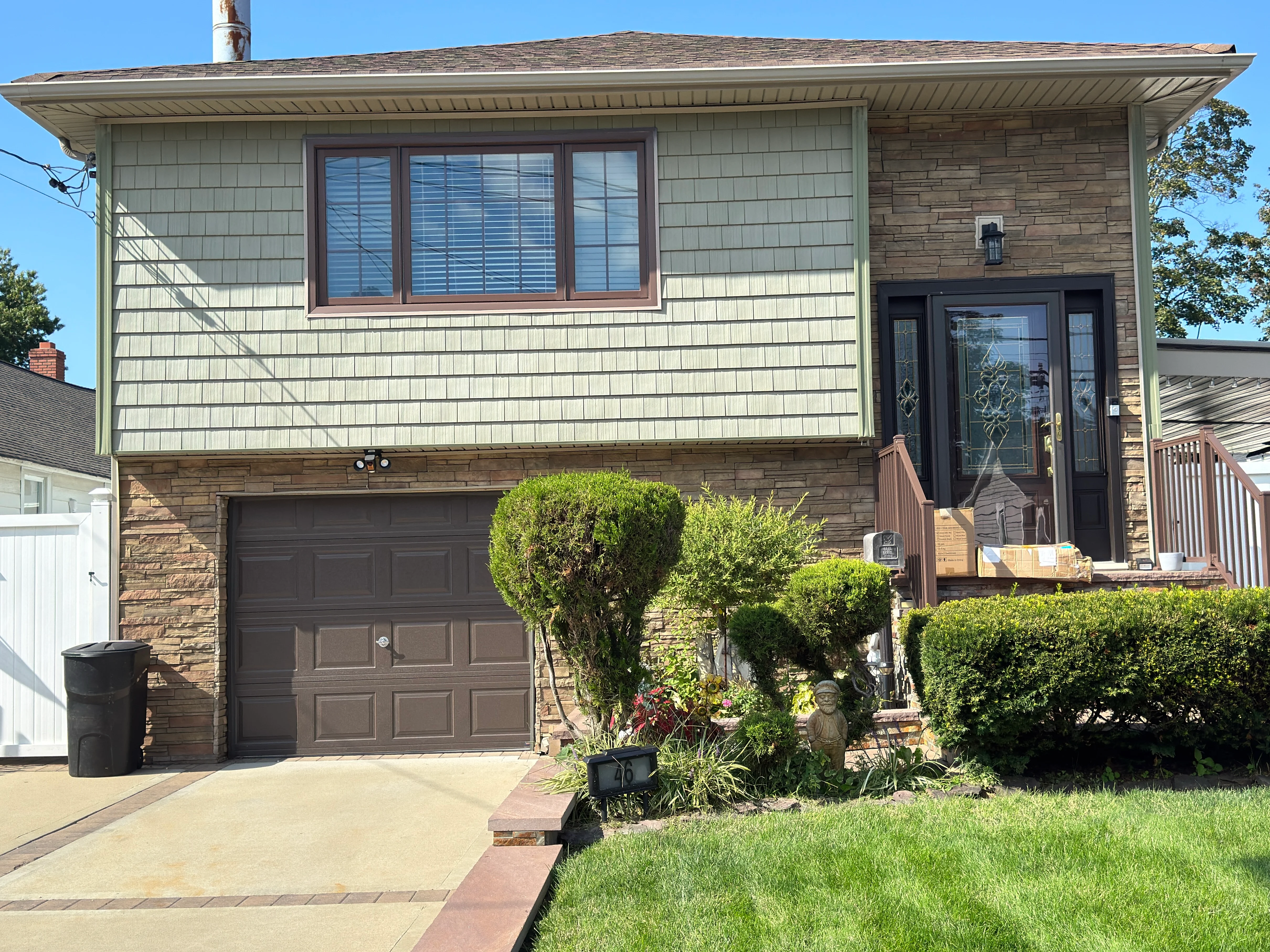 Split-level home with new cream siding, stone veneer, and dark garage door in Lindenhurst