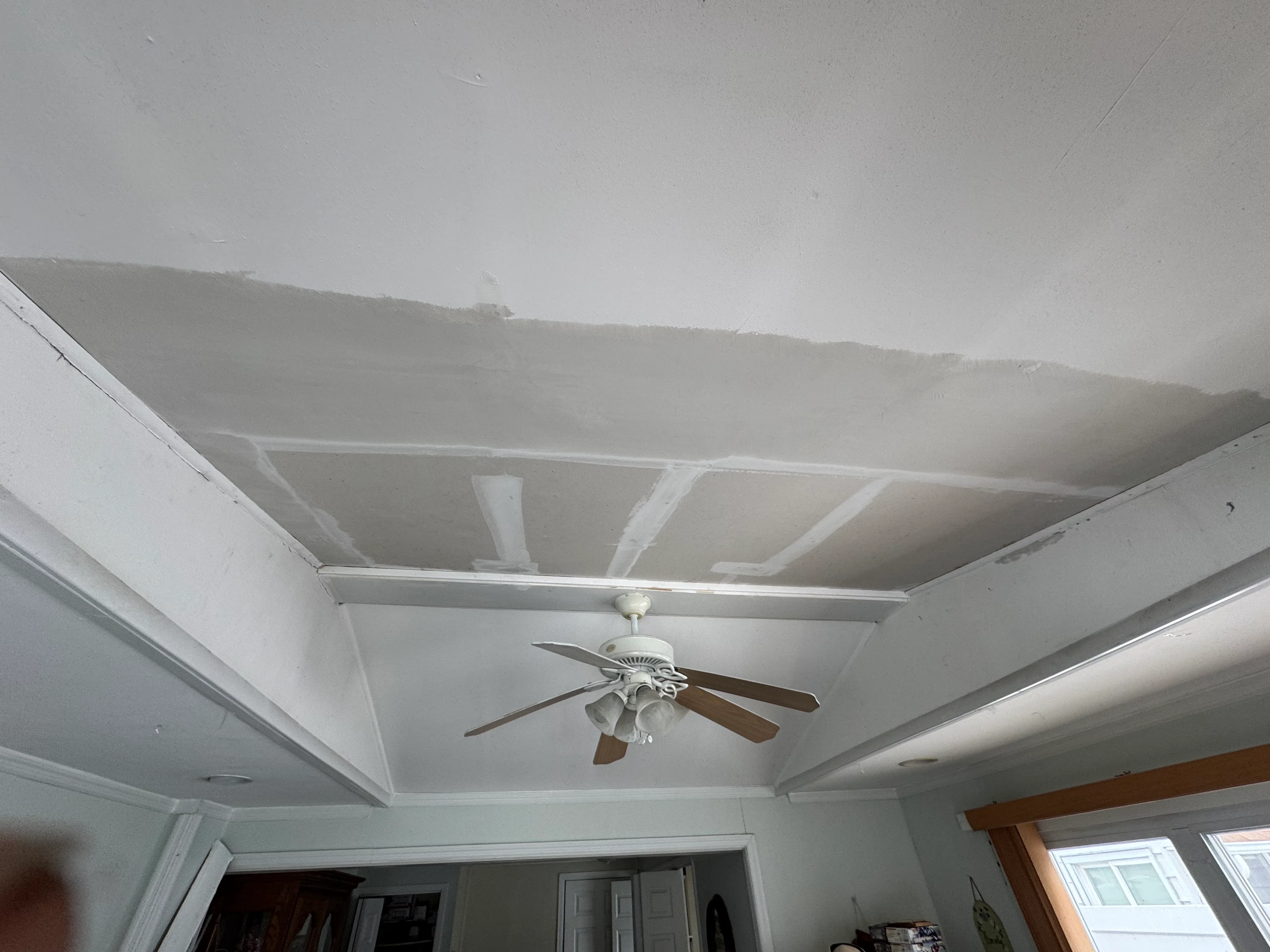 Newly installed drywall ceiling with taped joints and ceiling fan mounted in white finish