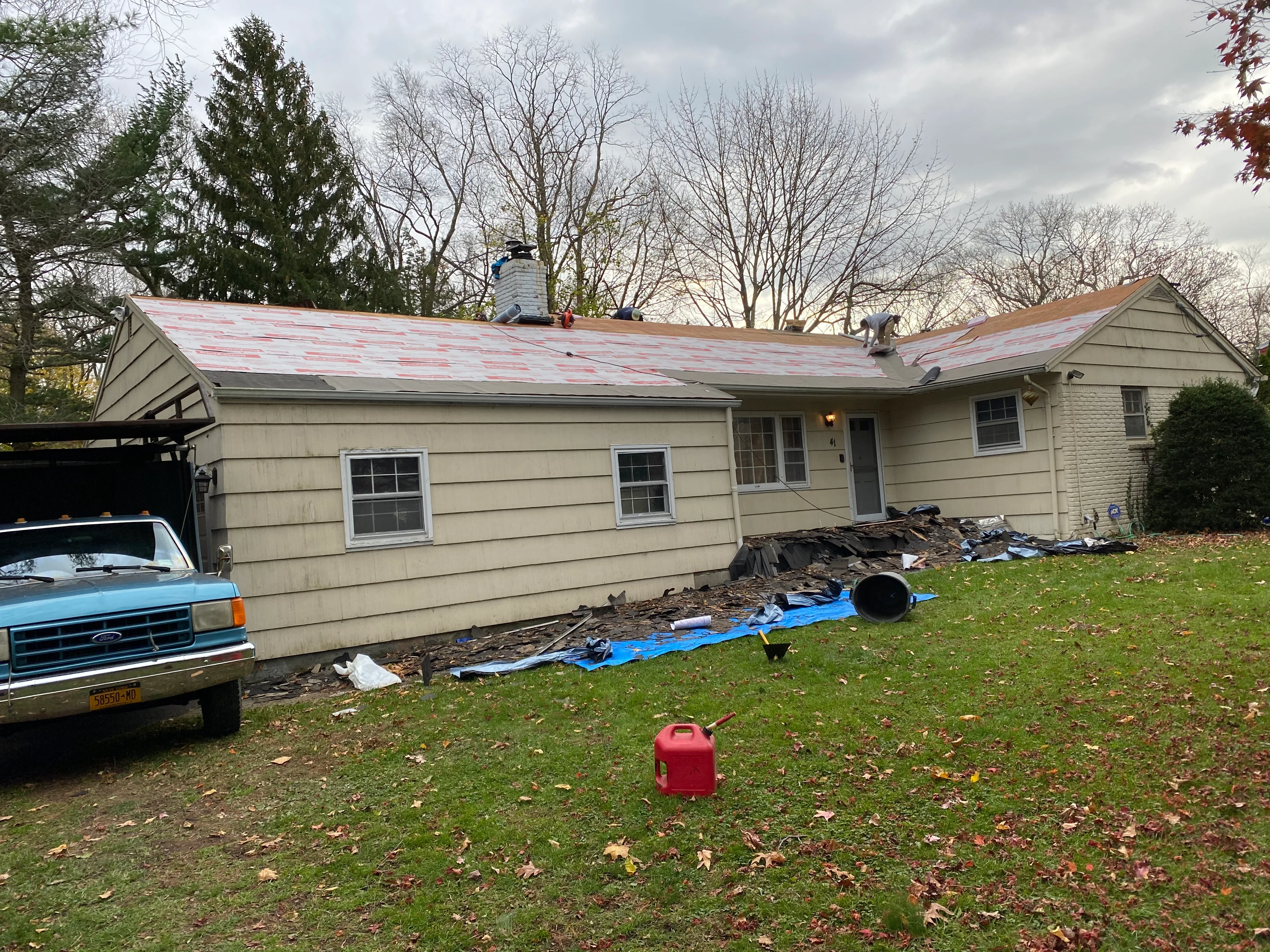 Ranch home with new roof installation in progress, showing exposed sheathing and protective tarps