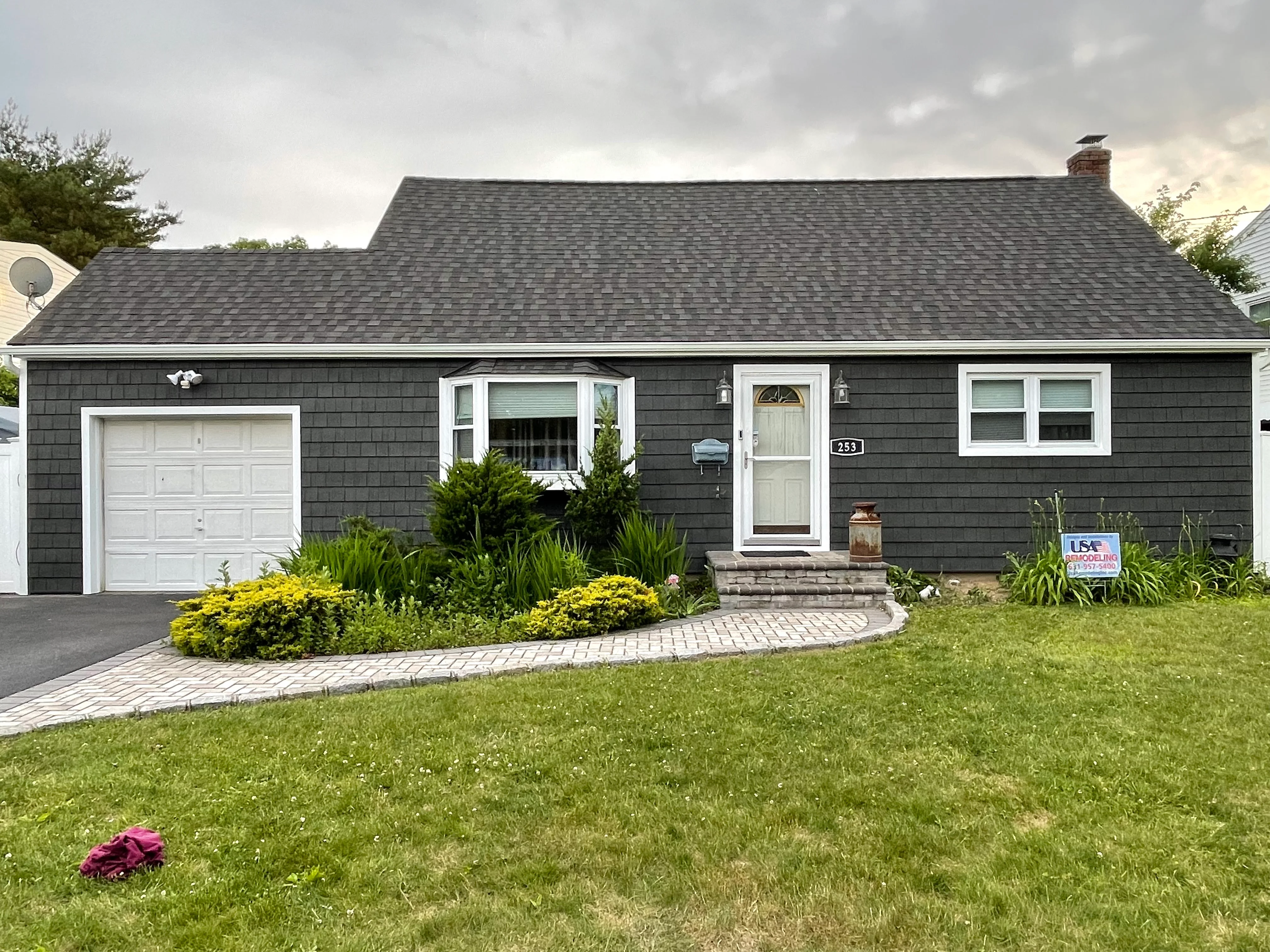 Renovated ranch home with dark siding, new roof, white trim, and curved paver walkway