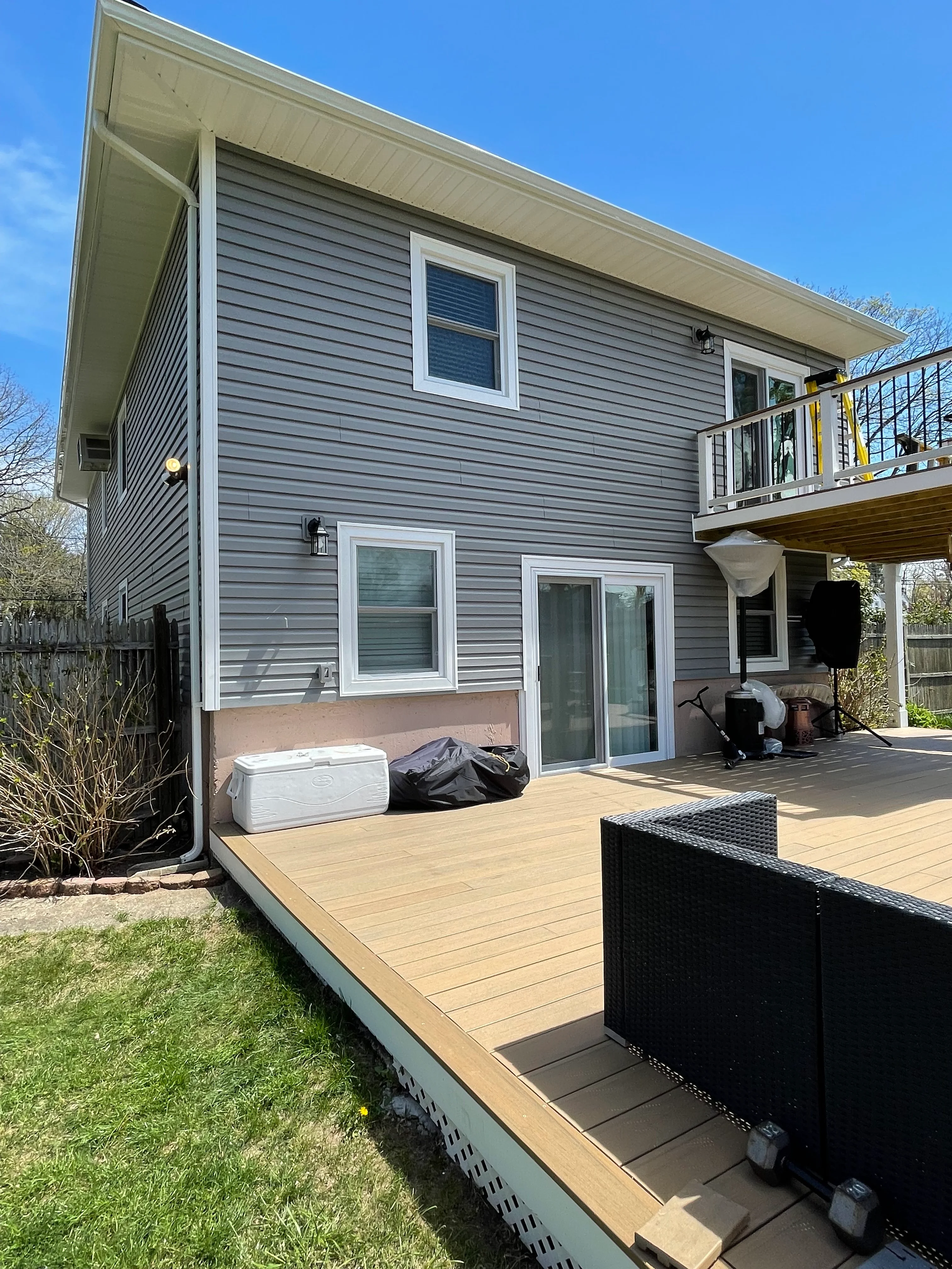 Two-story home with gray siding, white trim windows, and composite deck overlooking backyard