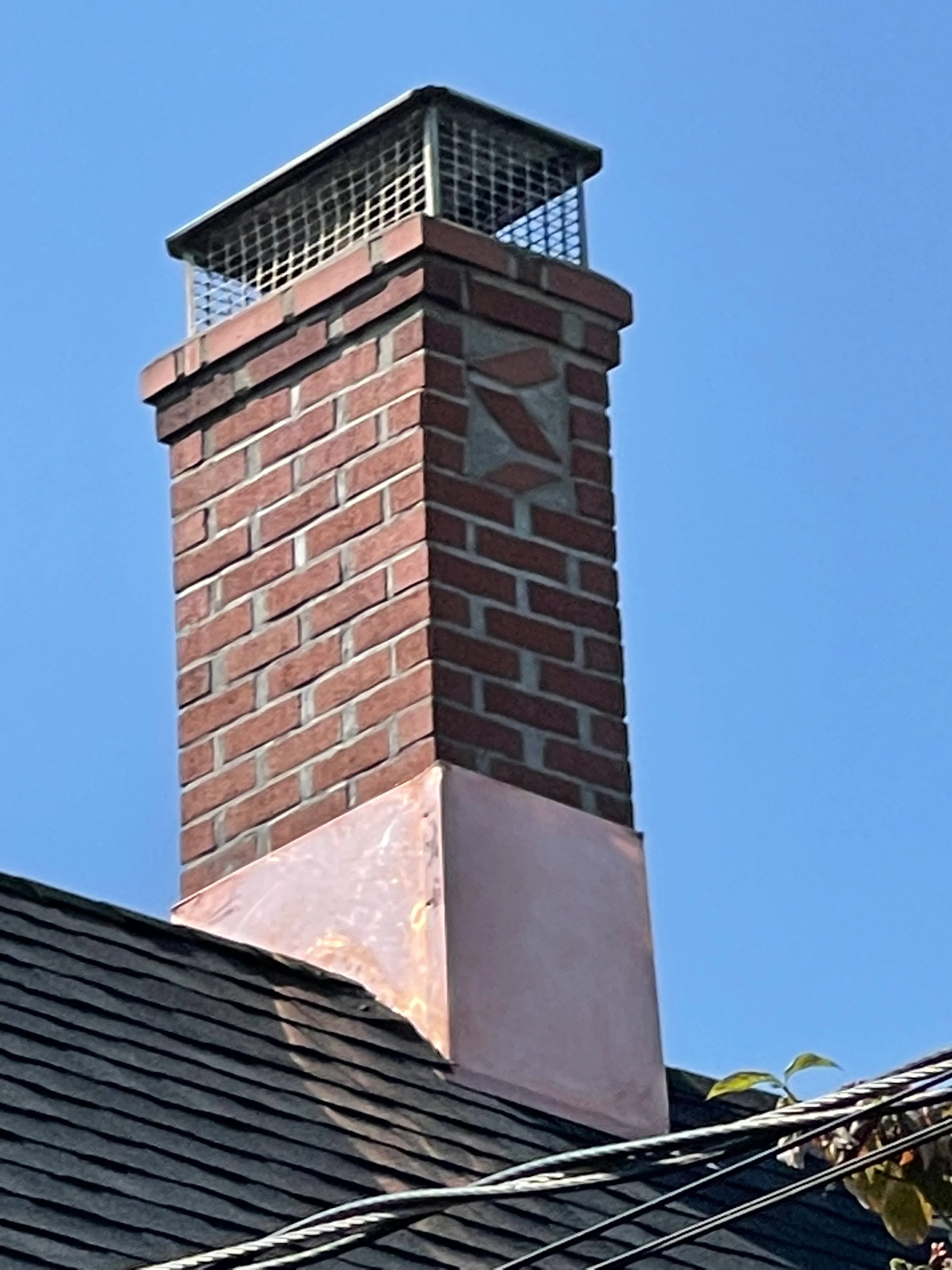 Restored brick chimney with new metal cap and mesh screening against clear blue sky