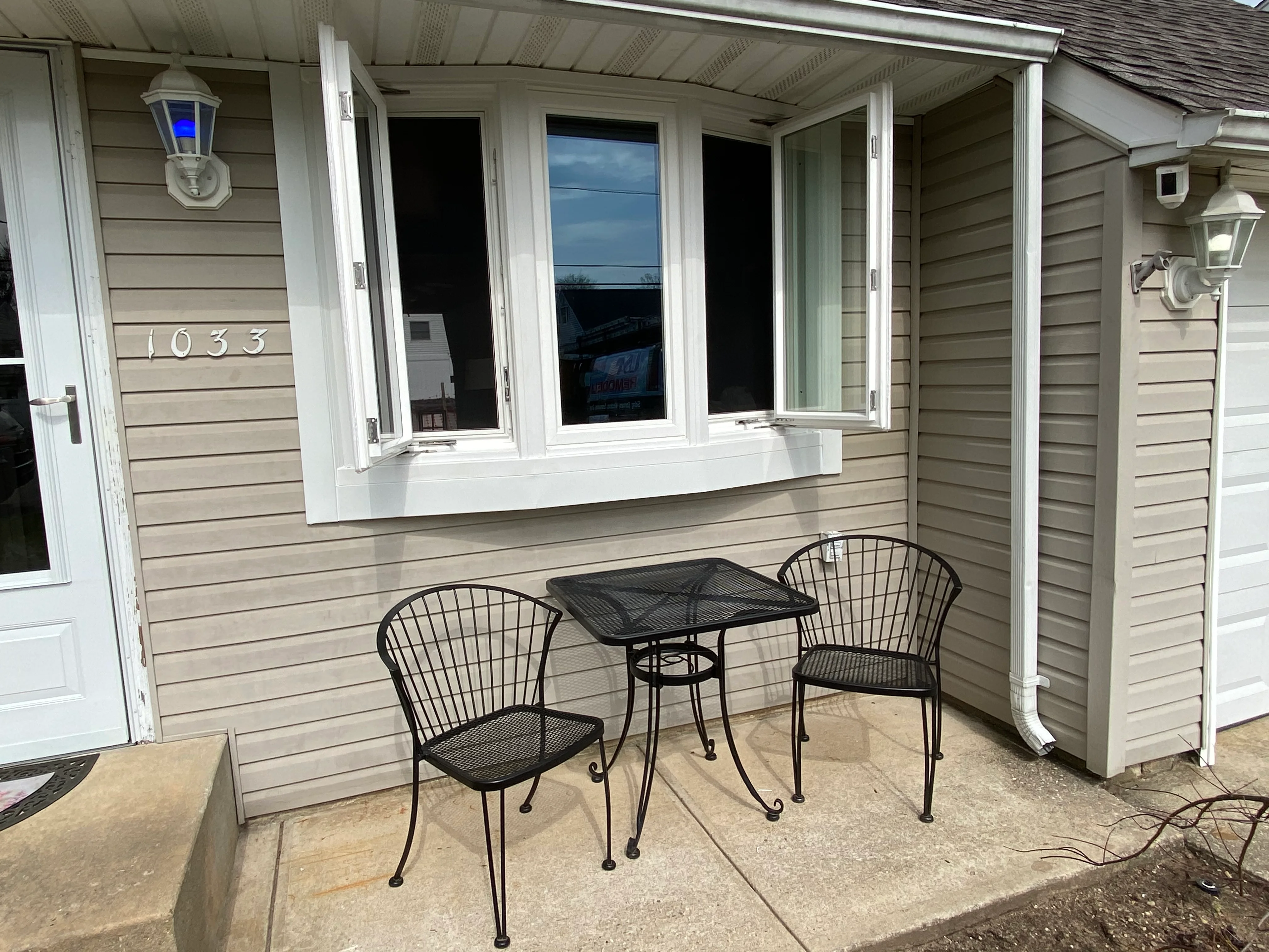 White vinyl window enclosure on tan siding porch with black metal seating