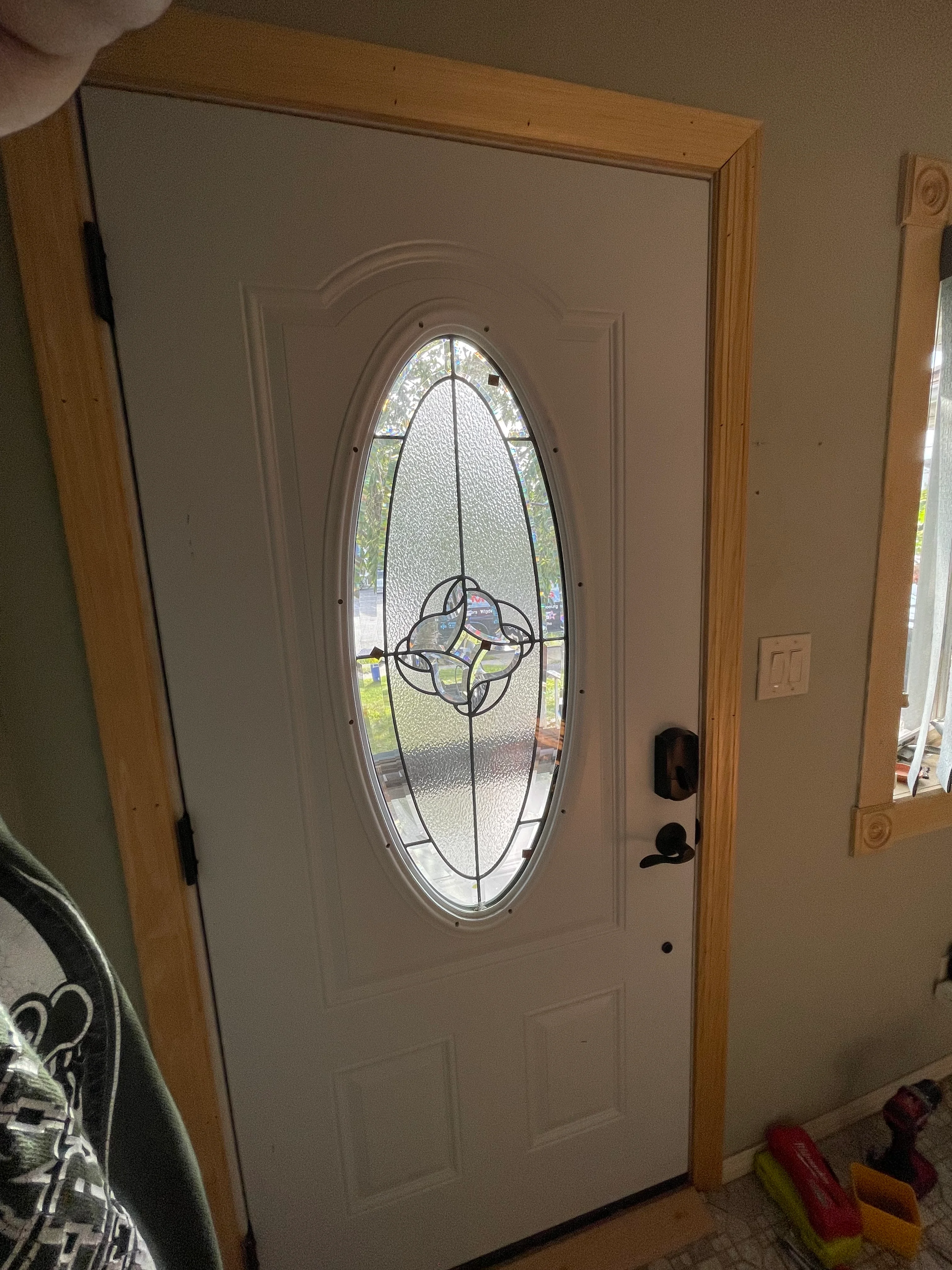White entry door with oval decorative leaded glass panel and geometric design in wood frame