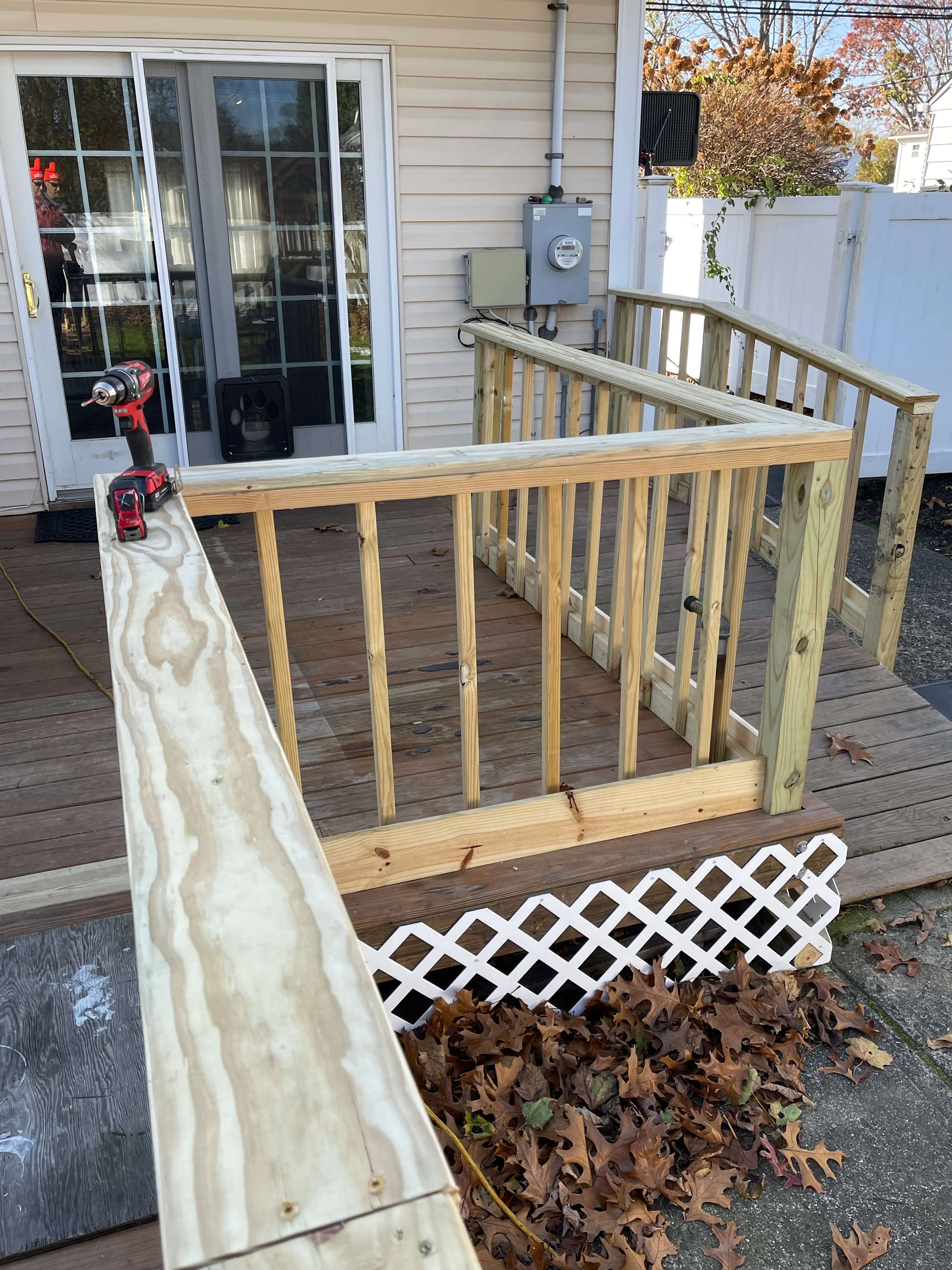 Newly installed wooden deck railing with vertical spindles and white lattice screening on composite deck