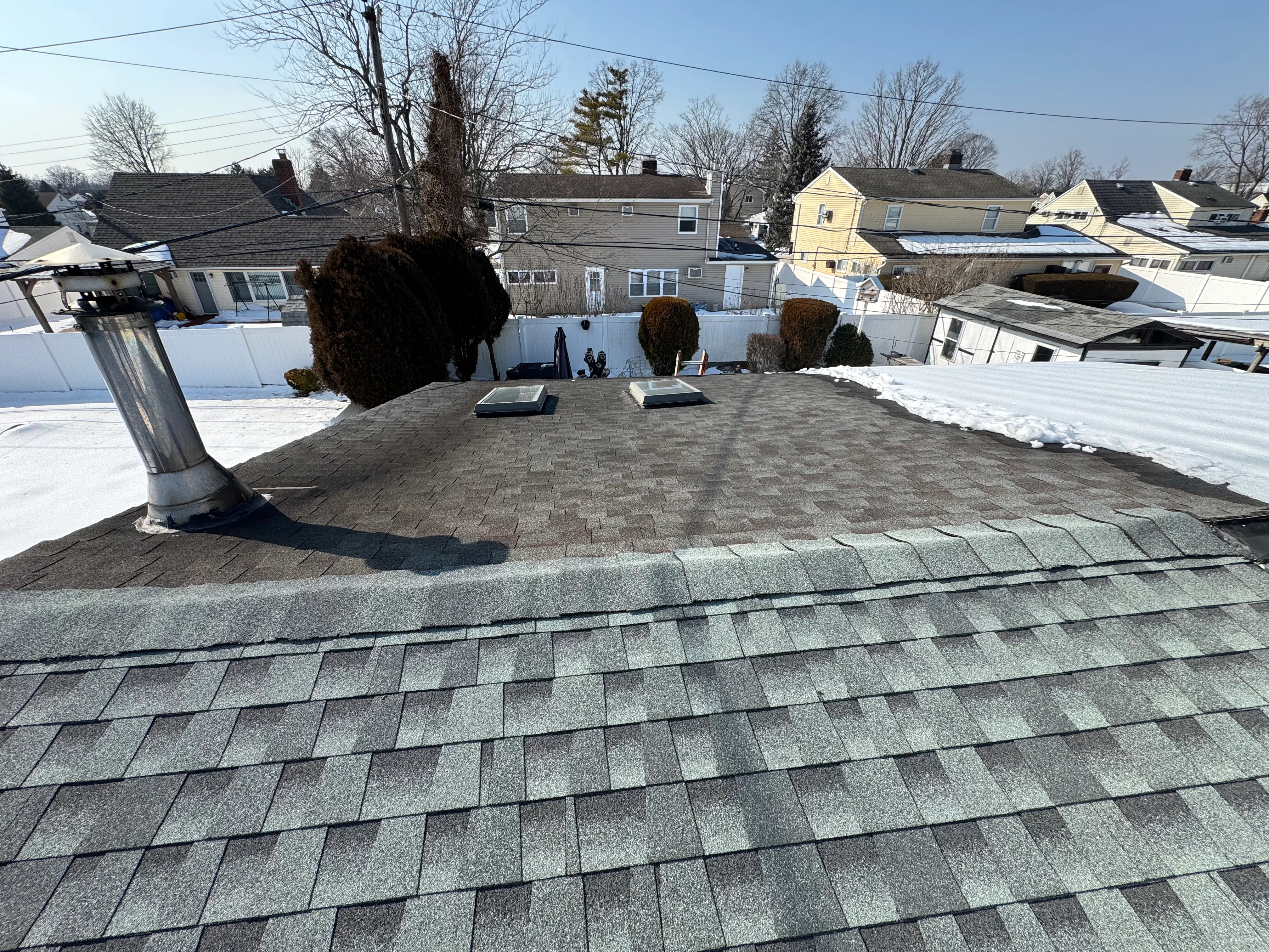 New gray architectural shingle roof installation on residential home with chimney and ridge vents visible