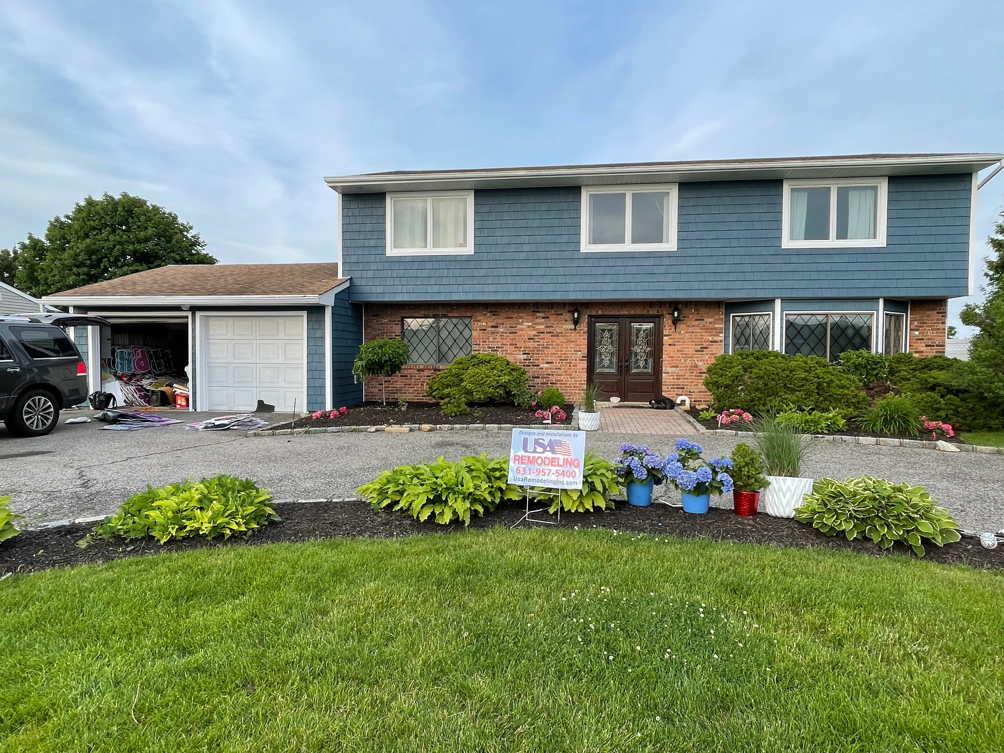 Split-level home with new blue siding, brick facade, white windows, and landscaped front beds