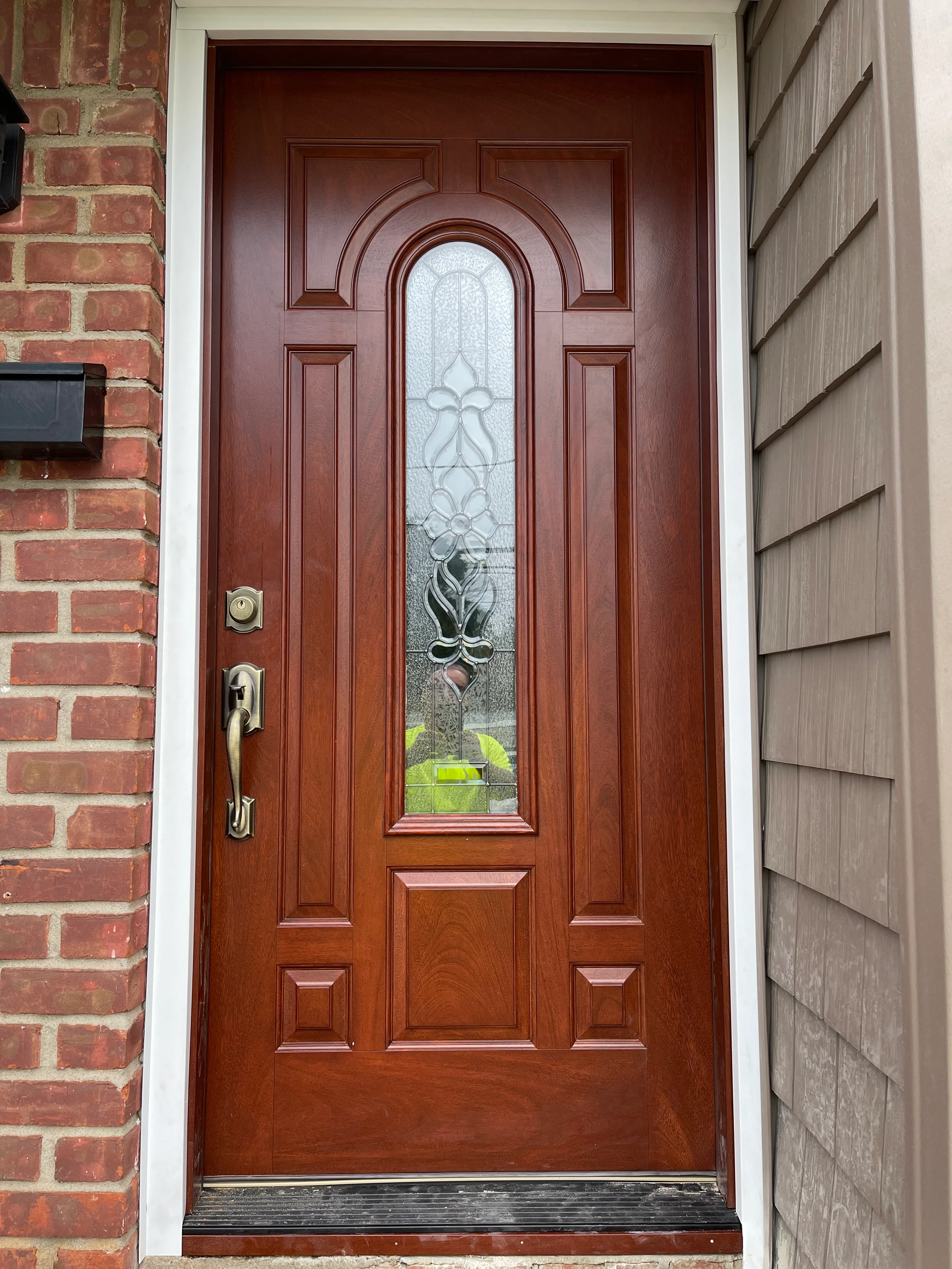 Rich mahogany entry door with arched glass transom and brass hardware on brick home